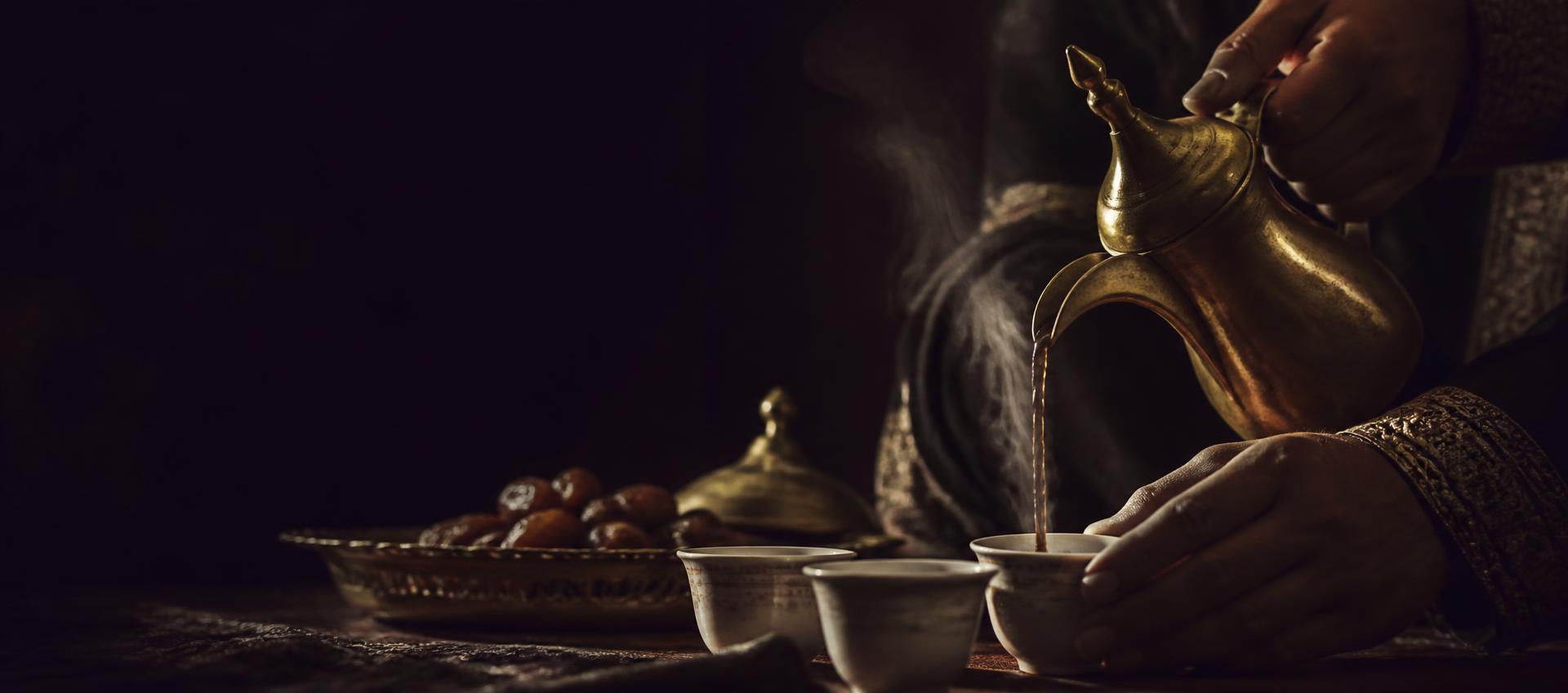 Yemeni coffee poured from a brass dallah into small cups by candlelight, the hospitality at the heart of The Birth of Coffee